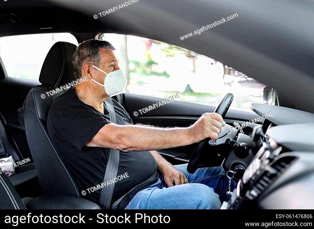 Senior in his 70s driving a car wearing face mask for protection against corona virus