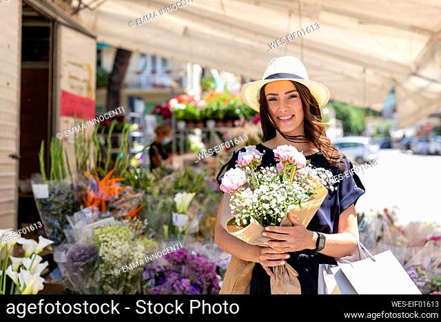Smiling woman holding bouquet of peonies flowers near florist shop