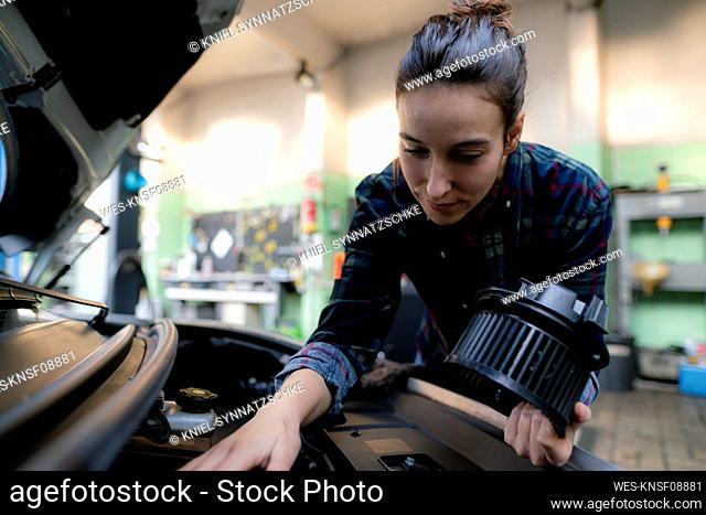 Female mechanic examining car engine at repair shop