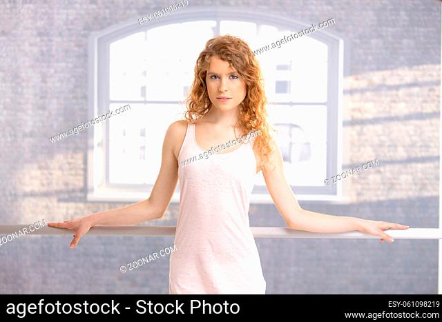 Pretty female dancer standing by bar in dance studio front of window