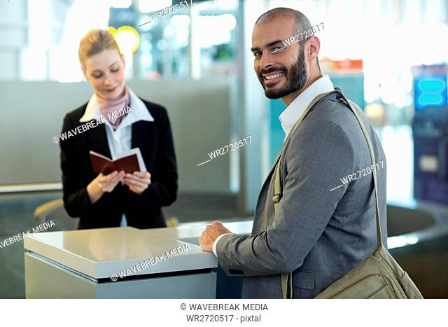 Smiling commuter standing at counter while attendant checking his passport