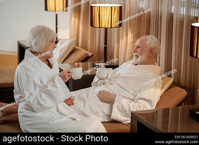 Morning. A senior couple in white robes having coffee and talking