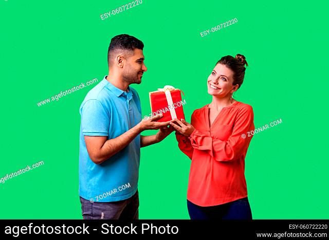 Couple celebrating Valentines day. Young handsome man in casual clothes giving box with present to beautiful elegant woman, looking at her with love