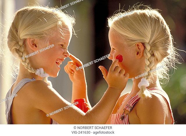portrait, close-up, profile of two laughing 5-year-old twin-girls with blond plaits wearing blue and red-white striped trousers with braces