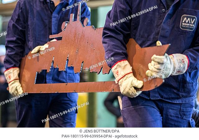 Two shipbuilders hold up a steel plate cut of in the relief of the expedition ship to be built during the official commencing ceremony for the start of...