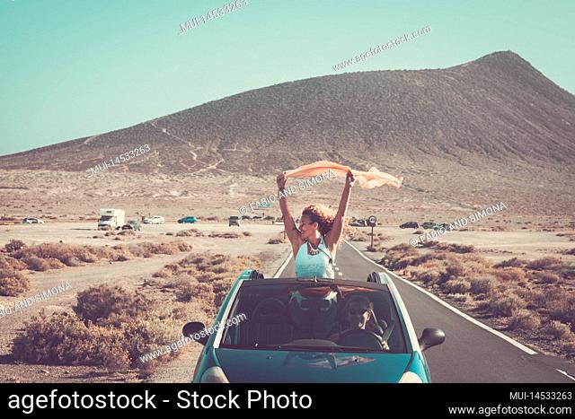 Travel and friendship concpet lifestyle. Adult woman overjoyed staying outside the roof of a convertible car while her friend drive smiling
