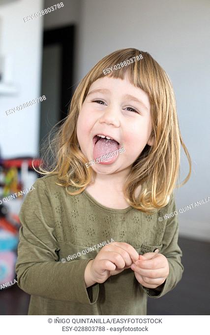 funny portrait of three years old child face, with green shirt and touching her finger, looking, laughing and sticking her tongue out