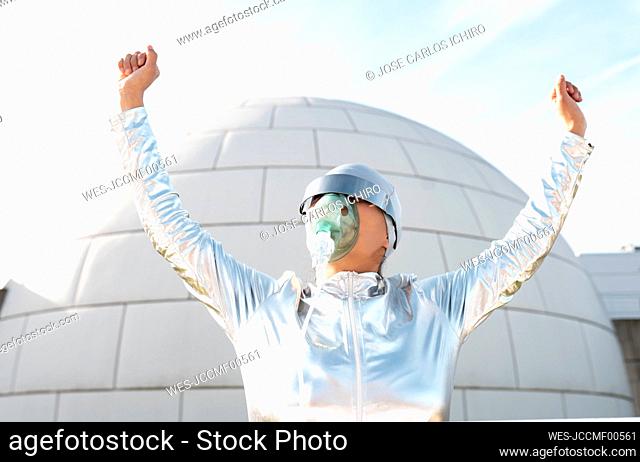 Woman in protective suit with oxygen mask and sunglasses cheering while standing against igloo
