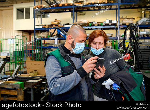 Industrial workers with face masks protected against coronavirus discussing production in the factory. People working during COVID-19 pandemic