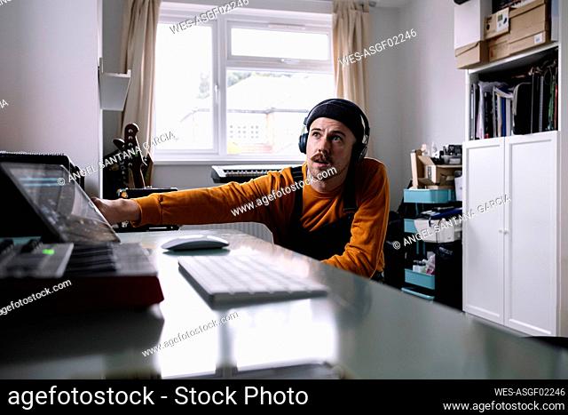 Freelancer wearing headphones sitting by table in home studio