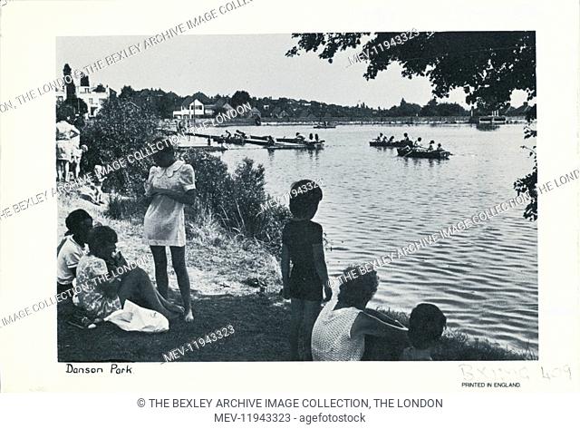 View of children and adults sitting beside the lake at Danson. People boating on the lake