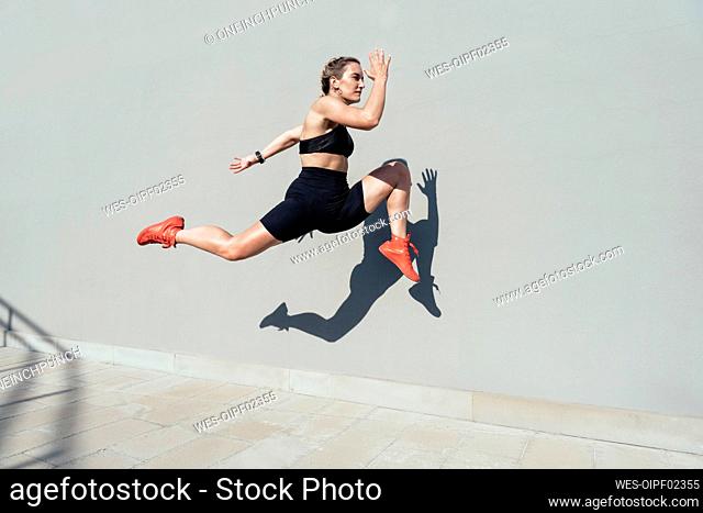 Young woman sprinting by wall on sunny day