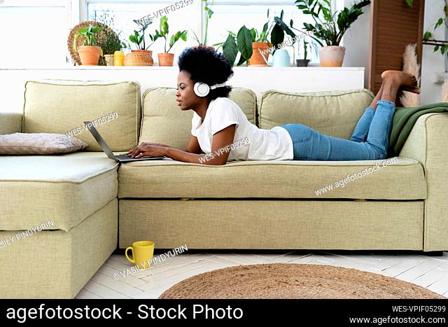 Young businesswoman with headphones using laptop on sofa at home