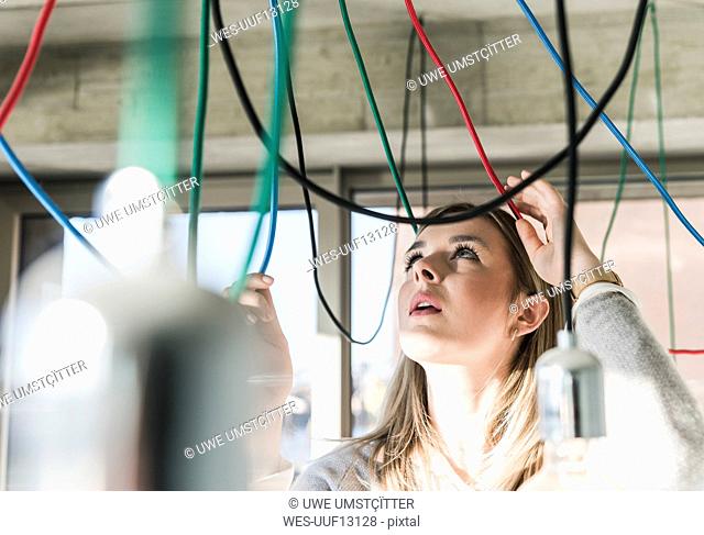 Young businesswoman in office examining cables at light bulbs