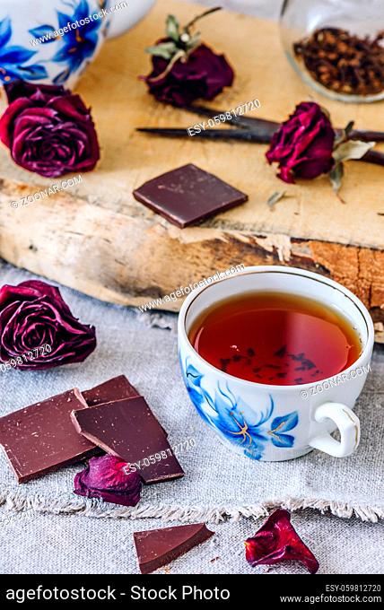 Cup of Black Tea with Chocolate Bars, Dry Rosebuds and Teapot with Jar and Rusty Scissors on Board. Vertical Orientation