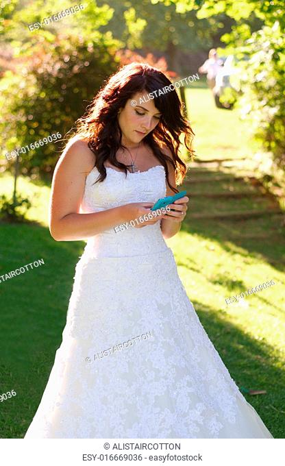 Bride texting on phone outside church on way to wedding