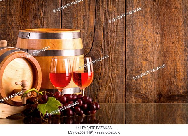 Glasses of rosé wine with two barrels grapes and dark wooden background