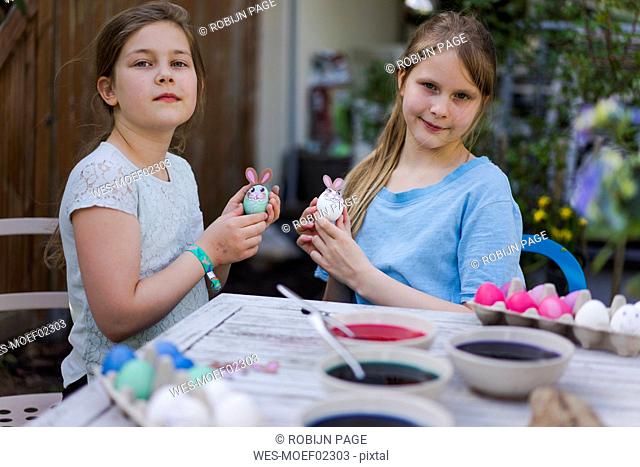 Portrait of two girls decorating Easter eggs on garden table