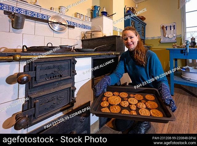 07 December 2023, Brandenburg, Frankfurt (Oder): Halina Muchow, museum educator, sits in ""Uroma's kitchen"" from the 1920s in the Viadrina Museum and shows...