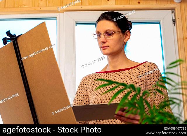 Portrait of an artist at work, a girl draws a drawing on an easel by the window