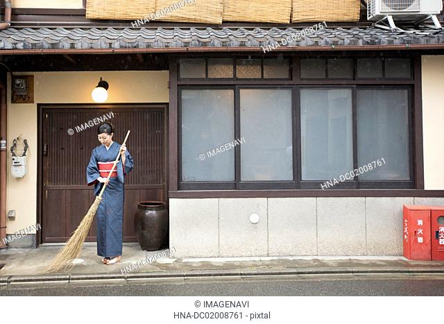 Mid Adult Japanese woman in kimono sweeping with broom