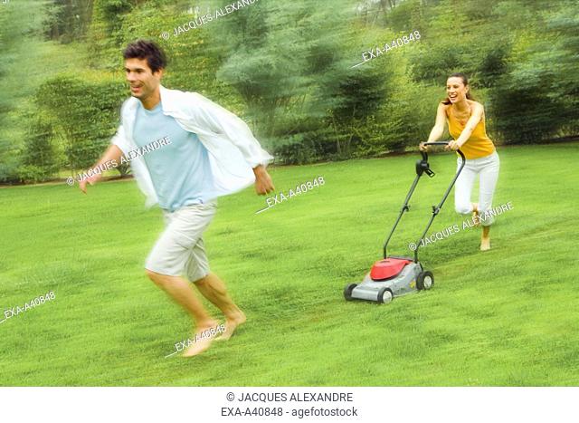 Young woman pushing mower while man running