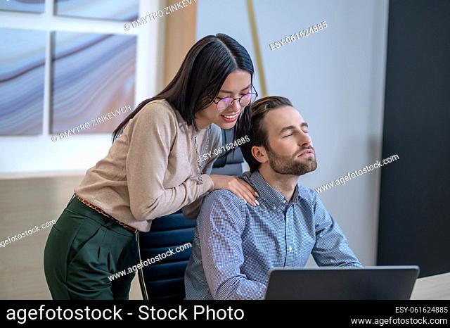 Smiling young female personal assistant massaging the shoulders of her male boss in his office