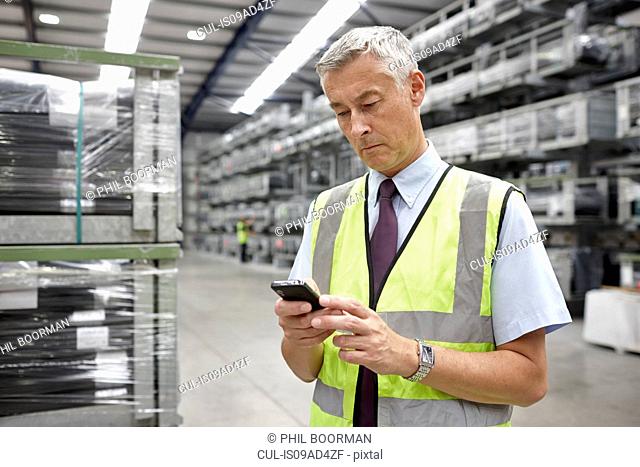 Portrait of manager using mobile phone in engineering warehouse