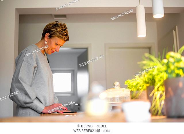 Woman using smartphone in kitchen at home