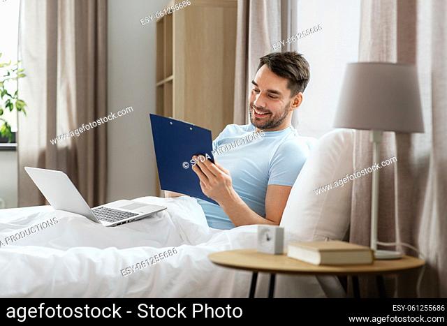 man with laptop working in bed at home bedroom