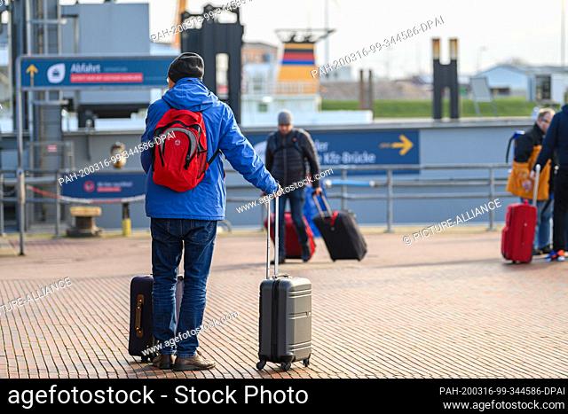 16 March 2020, Lower Saxony, Norddeich: Travellers walk with their suitcases at the ferry port of Norddeich. As of this Monday