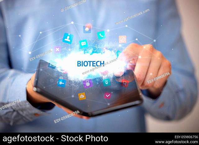 Businessman holding a foldable smartphone with BIOTECH inscription, technology concept
