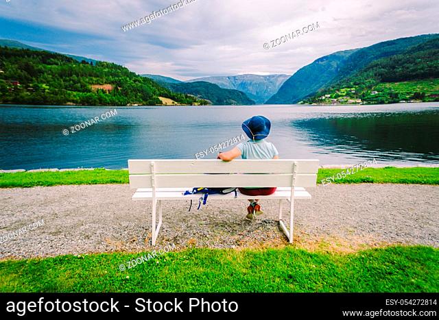 Woman sitting on a bench looking at the fjord in Ulvik, Norway. Fjord coastal promenade in Ulvik, Hordaland county, Norge