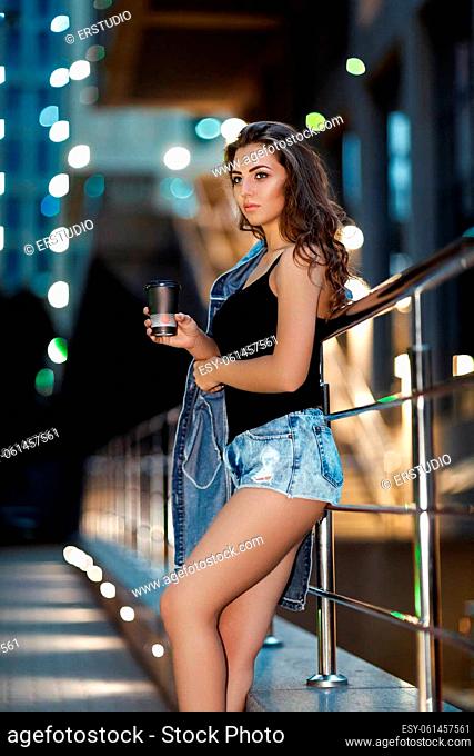 beautiful fashionable young woman with coffee in night city