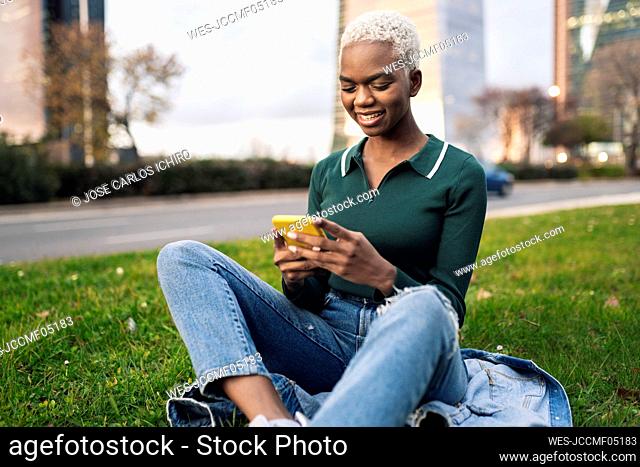 Young woman using smart phone sitting on grass at roadside