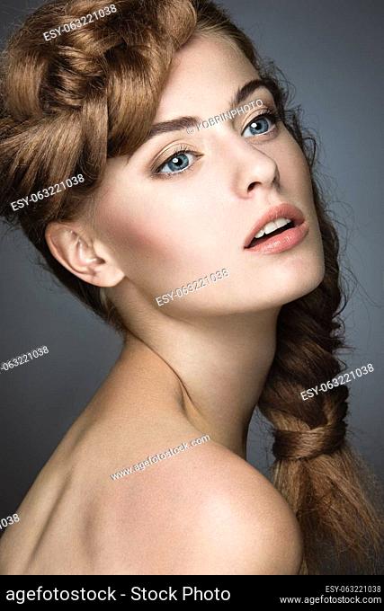Beautiful girl with light make-up, perfect skin and hairstyle as a braid. Picture taken in the studio on a gray background