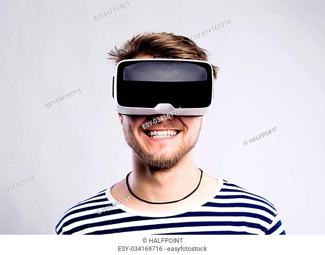 Hipster man in striped black and white sweatshirt wearing virtual reality goggles. Studio shot on gray background
