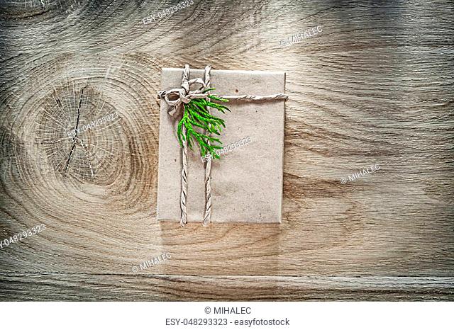 Handmade gift box wrapped in brown paper with green branch on wooden board