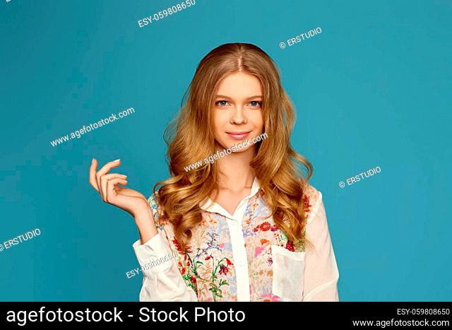 beautiful young curly blonde woman pointing to the side on blue background