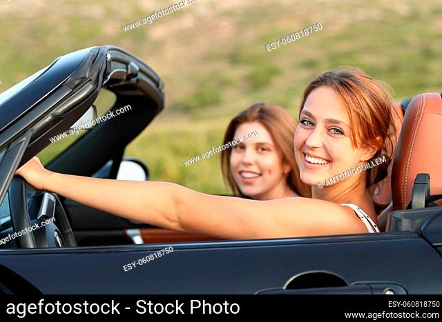 Two happy friends looking at you in a convertible car in the mountain