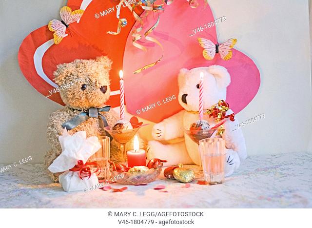 RagTag Teddy Bear has a present for White Teddy Bear  Curly-haired brown teddy bear with a blue ribbon sits with a white teddy bear with gold and red ribbon...