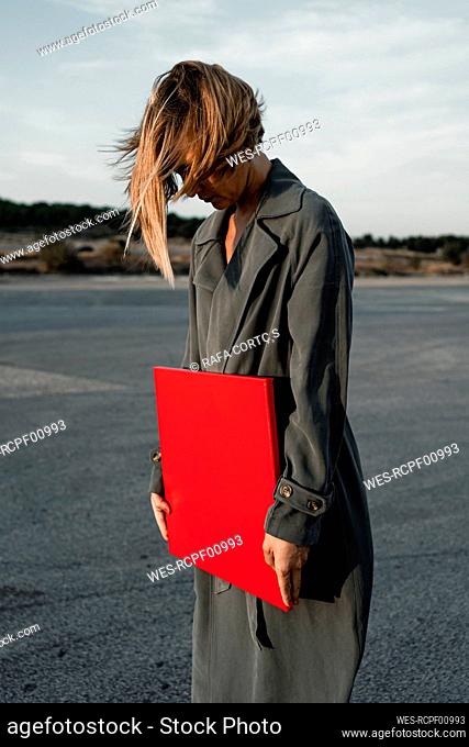 Woman with tousled hair holding red placard while standing at road