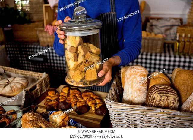 Mid section of staff holding glass jar of cookies at counter