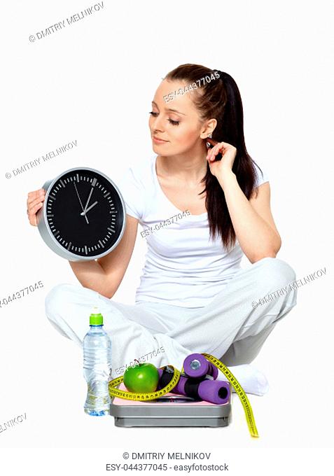 Sporty young woman with clock, scales, dumbbells and apple on a white background. Time for slimming