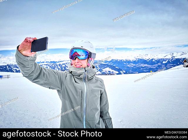 Smiling female snowboard taking a selfie with her smartphone