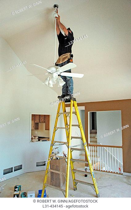 Electrician installing fans, lights, circuit panels and breakers on ladder