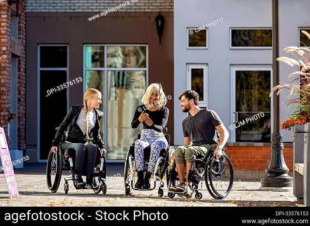 Three young paraplegic friends spending time together shopping and using a smart phone outside in a city area; Edmonton, Alberta, Canada