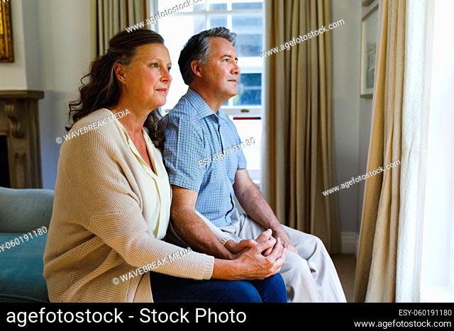 Happy senior caucasian couple sitting on sofa and holding hands