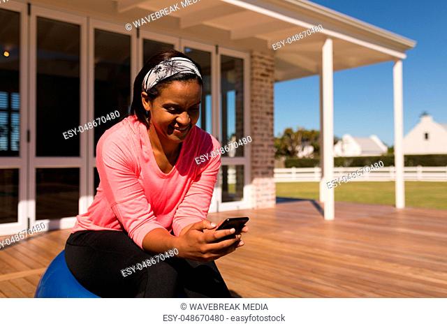 Woman using mobile phone while sitting on exercise ball in the backyard