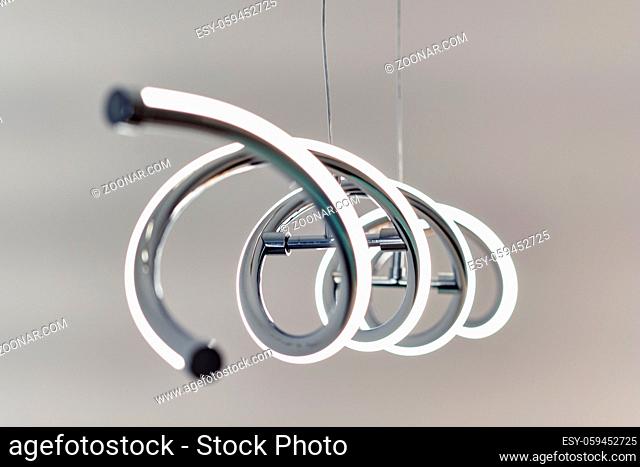 Close up of modern led pendant lamp lighting on hanging on ceiling over grey wall background, unusual shape design spiral form